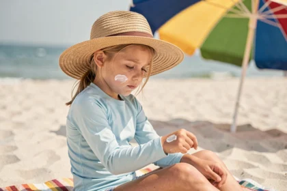 Jeune fille à la plage appliquant de la crème solaire sous un chapeau de paille pour se protéger des UV dangereux